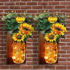 two mason jars with sunflowers are hanging from the side of a brick wall