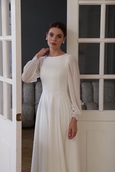 The Gabriella wedding dress combines elegance and modesty with its high neckline, long bishop sleeves, and flowing chiffon skirt. Ideal for brides seeking a timeless and graceful look, this dress features a modest design with a high neck, covered back, and bishop sleeves finished with delicate lace cuffs. Made from lightweight, airy chiffon, it offers effortless movement and comfort. The elegant A-line skirt flows into a soft train, adding a touch of romance to the overall silhouette. Perfect for weddings in any season, the Gabriella dress provides both coverage and style. Name: Gabriella Color: off white Bodice: chiffon, lining Sleeves: chiffon, lace Skirt: chiffon, lining Train: 12" / 30cm 💍 Check more than 1500 real brides' reviews and photos: piondress.com/reviews/ Sizes ▪️ Standard s Modest White Dresses, Apostolic Wedding Dress, Modest White Dress, Modest Wedding Dresses Lds, Boat Neck Wedding Dress, Wedding Dresses Lds, Chiffon Wedding Gowns, Skirt Chiffon, Modest Wedding Gowns