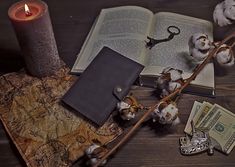 an open book sitting on top of a wooden table next to a candle and money