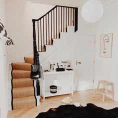 a living room filled with furniture and a stair case next to a white wall on top of a hard wood floor