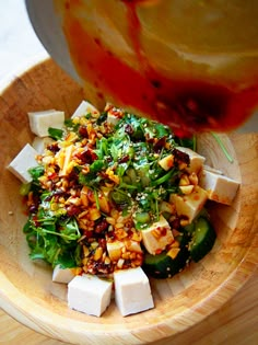 a wooden bowl filled with vegetables and tofu on top of a table next to sauce