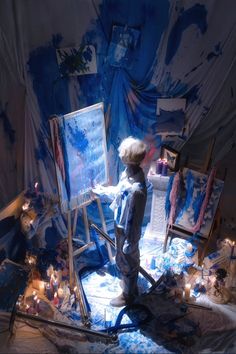 a young boy painting on an easel in front of a blue backdrop with candles