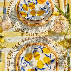 two yellow and blue plates sitting on top of a table next to glasses, silverware and utensils