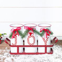 four white cups with red bows and candy canes in them on a sled