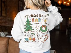 a woman wearing a white sweatshirt with the words jesus is nativity and christmas decorations