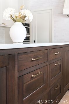 a white vase with flowers on top of a wooden cabinet in a room that has white walls and floors