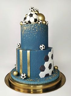 a three tiered blue cake with soccer balls on top and gold trimmings