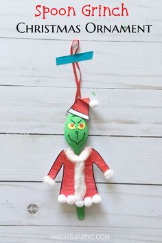 the grinch ornament is hanging on a white wooden wall with a blue ribbon