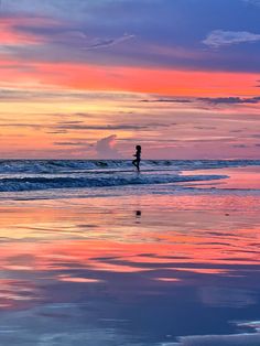 a person standing on top of a surfboard in the ocean under a colorful sky