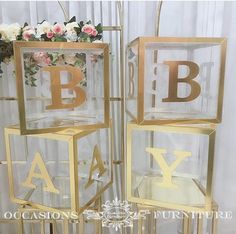 two gold and clear glass boxes with letters on them sitting side by side in front of a white curtain