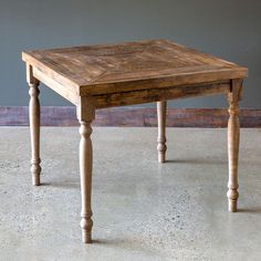 a small wooden table sitting on top of a cement floor next to a gray wall