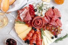 an assortment of cheeses, meats and fruits on a platter with wine glasses