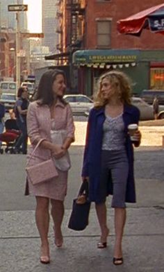 two women walking down the street talking to each other and one is holding a purse