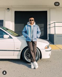 a man standing next to a white car in front of a garage with his hands on his hips