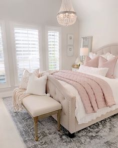 a bedroom with a large bed, chandelier and two windows that have white shutters