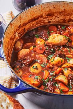 a pot filled with meat and vegetables on top of a table next to toasted bread