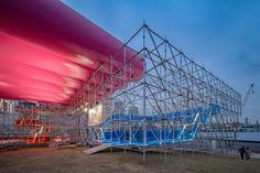 a large structure with blue and red seats on it's sides in front of a body of water