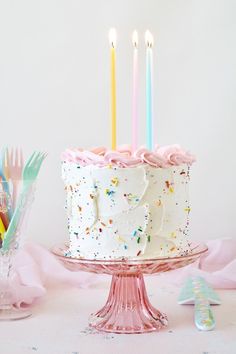 a birthday cake with white frosting and sprinkles is on a pink pedestal