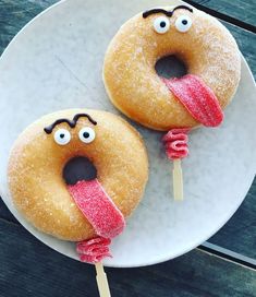 two donuts with sticks sticking out of them on a white plate and wooden table