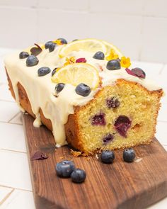 a loaf of lemon blueberry bread on a wooden cutting board with fresh fruit and icing