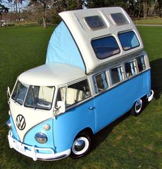 a blue and white vw bus parked on top of a grass covered field next to trees