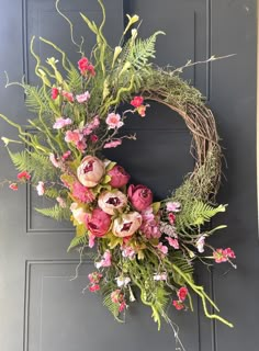 a wreath with pink flowers and greenery hanging on a door