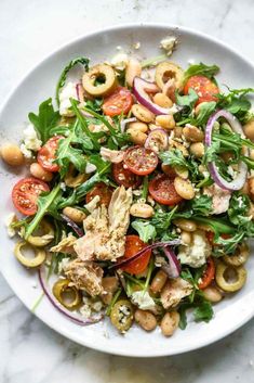 a white bowl filled with salad and lots of vegetables on top of a marble table