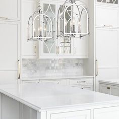 a kitchen with white cabinets and marble counter tops, an island in the middle is flanked by two chandeliers