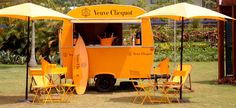 an orange food truck with yellow chairs and umbrellas on the grass in front of it