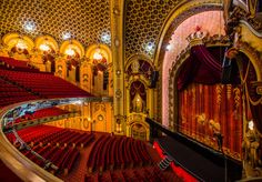 an empty auditorium with red seats and gold walls, looking down at the stage from the balcony