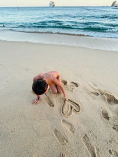 a woman is writing in the sand at the beach