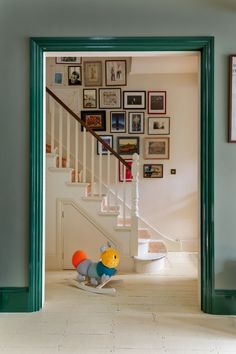 an open door leading to a hallway with pictures on the wall and a stuffed animal