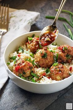 a white bowl filled with meatballs and rice on top of a table next to silverware