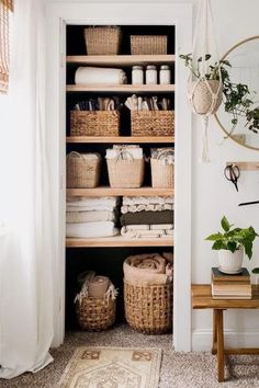 an open closet with baskets and towels on the shelves next to a table, mirror and rug