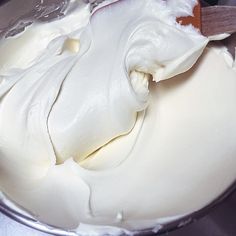 a bowl filled with white frosting sitting on top of a metal counter next to a wooden spoon