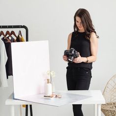 a woman standing in front of a white table holding a camera