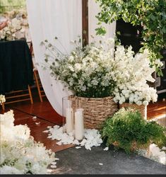 white flowers and greenery are in baskets on the floor next to a table with candles