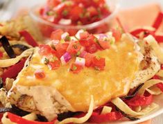 a white plate topped with meat and veggies covered in cheese sauce next to a bowl of salsa