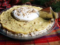 a pie with whipped cream and pecans on top is sitting on a plaid tablecloth