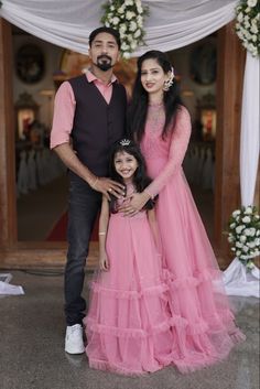 a man and woman pose for a photo with their daughter in front of a wedding arch