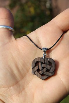 a hand holding a wooden heart pendant on it's string with an arrow in the middle