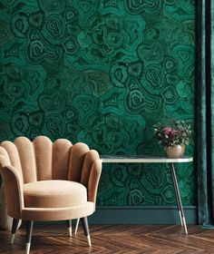 a chair sitting in front of a table with a vase on it and green wallpaper