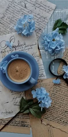 a cup of coffee sitting on top of a table next to some papers and flowers