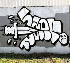 graffiti is painted on the side of a concrete wall in front of a grassy area