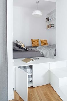 a bed sitting under a window next to a white shelf filled with pillows and blankets