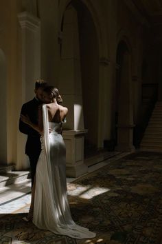 a bride and groom standing in an old building with sunlight streaming through the windows on their backs