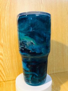 a blue glass sitting on top of a white pedestal next to a wooden wall and floor