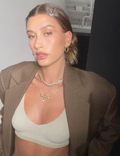 a woman in a tan jacket and white top posing for the camera with her hand on her hip