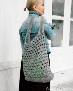 a woman carrying a crocheted bag in front of a white building with windows