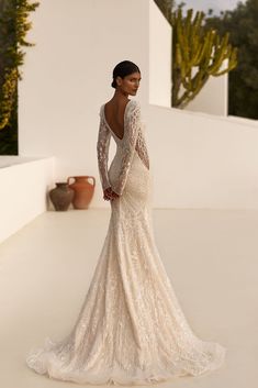 a woman in a wedding dress standing on a white surface with cactuses behind her